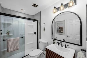 Contemporary bathroom with arched mirror, walk-in glass shower, toilet, and dark wood vanity.