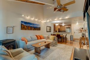 Spacious living room with sectional sofa, track lighting, ceiling fan, beamed ceiling, and mountain landscape artwork.