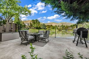 Spacious patio with outdoor dining furniture and grill overlooking a peaceful lake with mountain backdrop.