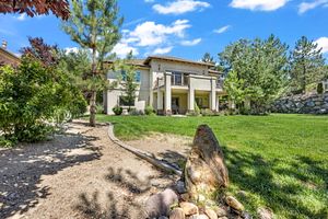 Elegant two-story home with a manicured lawn, stone pathway, and towering pine trees in the backyard.