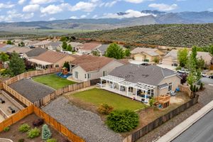 Aerial view of single-story home with green backyard, covered patio, play area, and mountain backdrop.