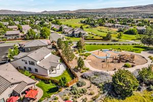 Aerial view of suburban homes bordering a golf course with a playground and desert mountain landscape.