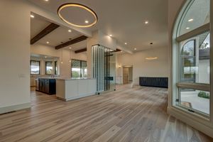 Spacious open-concept living area with light hardwood floors, exposed wood beams, circular ceiling detail, and glass wine display.