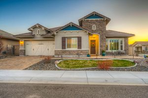 Charming craftsman home with stone facade, paver driveway, and warm glowing entry at twilight with colorful sunset sky.