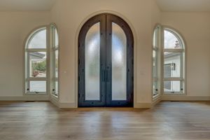 Grand entryway featuring an arched dark wood double door with frosted glass panels and matching arched sidelights on hardwood floors.