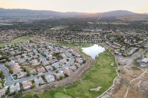 Aerial view of suburban neighborhood with golf course, pond, and mountain backdrop at sunset.