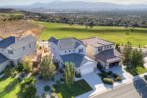 Aerial view of two-story suburban homes adjacent to a lush green golf course with mountain views.