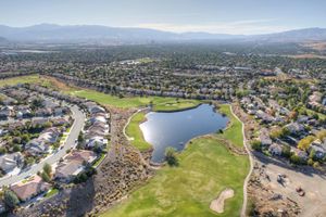 Aerial view of a golf course community with a pond, surrounded by suburban homes and mountain backdrop.