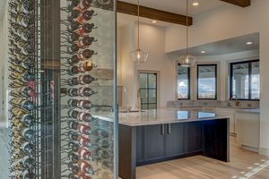 Floor-to-ceiling glass wine storage wall beside a kitchen island with dark cabinetry, marble countertop, and pendant lighting.