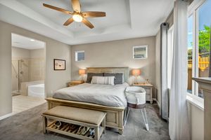 Elegant master bedroom with tray ceiling, ceiling fan, bench, and en-suite bathroom with natural light.