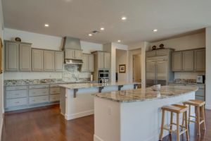 Spacious kitchen with gray cabinetry, granite island, stainless appliances, and hardwood floors.