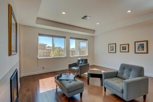 Bright sitting room with hardwood floors, gray chairs, fireplace, and large windows.
