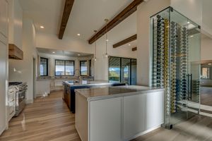 Open kitchen with white and dark cabinetry, marble island, exposed wood beams, glass wine wall, and panoramic windows.