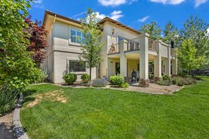 Two-story stucco home with a lush green lawn, balcony, and beautifully landscaped front yard with trees.
