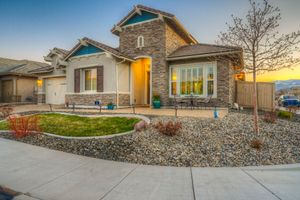 Craftsman home exterior featuring stone tower, teal trim, xeriscape landscaping, and mountain views at sunset.