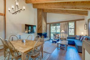 Rustic cabin dining room with wood beam ceiling, chandelier, and open living area.