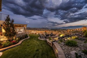 Landscaped backyard with curved lawn, stone retaining walls, and city lights at dramatic dusk.