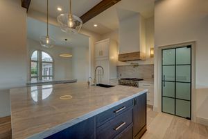 Modern kitchen island with thick marble countertop, dark navy cabinets, gold faucet, and custom range hood with exposed wood beam.