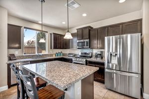 Modern kitchen with dark cabinetry, granite island, stainless steel appliances, pendant lights, and tile flooring.