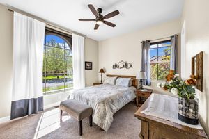 Spacious bedroom with carpet, ceiling fan, large windows with natural light, and wood furniture accents.
