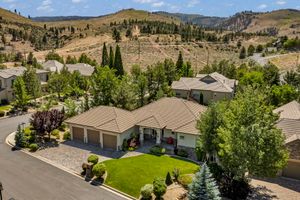 Aerial view of a single-story home with a three-car garage, green lawn, and mountain backdrop.
