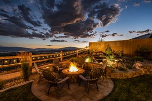 Backyard patio with fire pit seating, string lights, water feature, and mountain views at night.