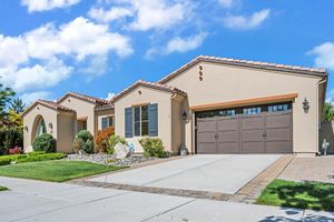 Spanish-style single-story home with stucco exterior, tile roof, two-car garage, and landscaped front yard.