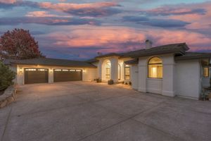 Stunning stucco home with arched windows, double garage, and vibrant pink and purple sunset sky backdrop.