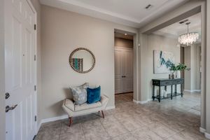 Bright entryway with neutral tones, decorative round mirror, accent chair, and elegant chandelier in background.