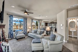 Spacious living room with gray sectional sofa, ceiling fan, carpet flooring, and open view into modern kitchen.