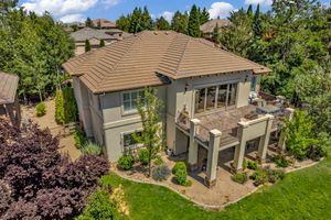 Aerial view of a two-story home with a pergola, lush landscaping, and mature trees surrounding the property.