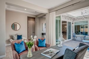 Stylish dining area with teal accent pillows, floral centerpiece, and sliding glass doors opening to lit patio.