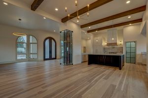 Expansive open living space with light hardwood floors, exposed wood beams, glass wine tower, and arched entryway doors.