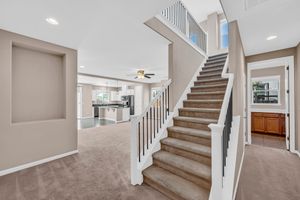 Bright open staircase with white railings leading to carpeted living area and modern kitchen beyond.