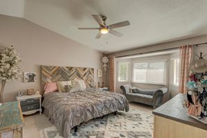 Spacious master bedroom with vaulted ceiling, ceiling fan, herringbone wood headboard, and large bright window.