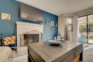 Cozy living room with brick fireplace, blue accent wall, mounted TV, and sliding glass doors leading to outdoor patio.
