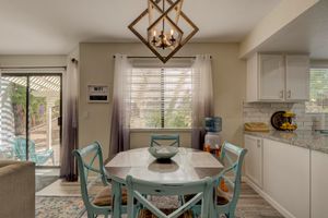 Bright dining area with teal chairs, round table, geometric chandelier, and sliding glass doors with natural light.