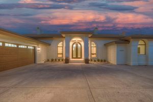 Elegant home entrance featuring arched doorway, double wood garage door, and vivid purple sunset sky.