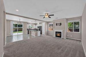 Spacious open-concept living room with fireplace, ceiling fan, and view into modern kitchen area.