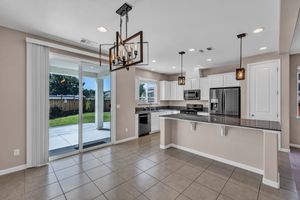 Modern kitchen with white cabinets, dark granite island, stainless appliances, and sliding glass door.