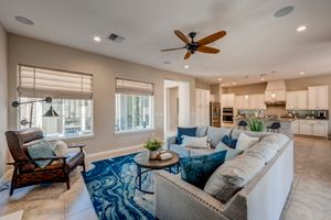 Open-concept living room with large sectional, ceiling fan, blue rug, and view into bright modern kitchen.