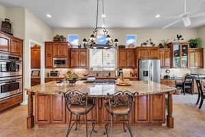 Spacious kitchen with cherry wood cabinets, granite island, bar seating, stainless appliances, and elegant chandelier.