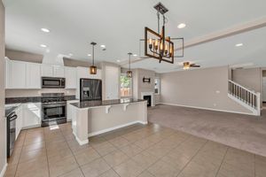 Open-concept kitchen with white cabinets, dark granite island, stainless appliances, and adjacent living room.