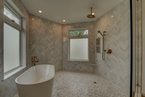 Luxurious master bathroom with herringbone tile walls, freestanding soaking tub, mosaic marble floors, and gold fixtures.