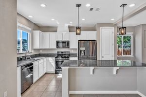 Modern kitchen with white cabinets, dark granite countertops, stainless steel appliances, and pendant lighting.