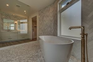 Elegant bathroom featuring a freestanding white soaking tub, herringbone tile walls, marble mosaic floors, and gold floor-mount faucet.
