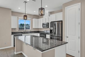 Bright kitchen featuring white cabinetry, dark granite island, stainless steel appliances, and pendant lights.