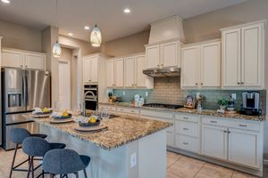 Gourmet kitchen with white cabinets, granite island, pendant lights, and stainless steel appliances.
