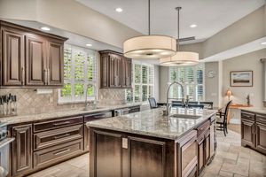 Gourmet kitchen with dark wood cabinets, granite island, pendant lights, and plantation shutters on windows.