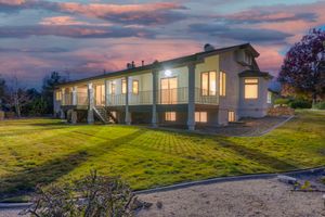 Two-story home with large deck, manicured green lawn, and stunning colorful sunset sky at dusk.